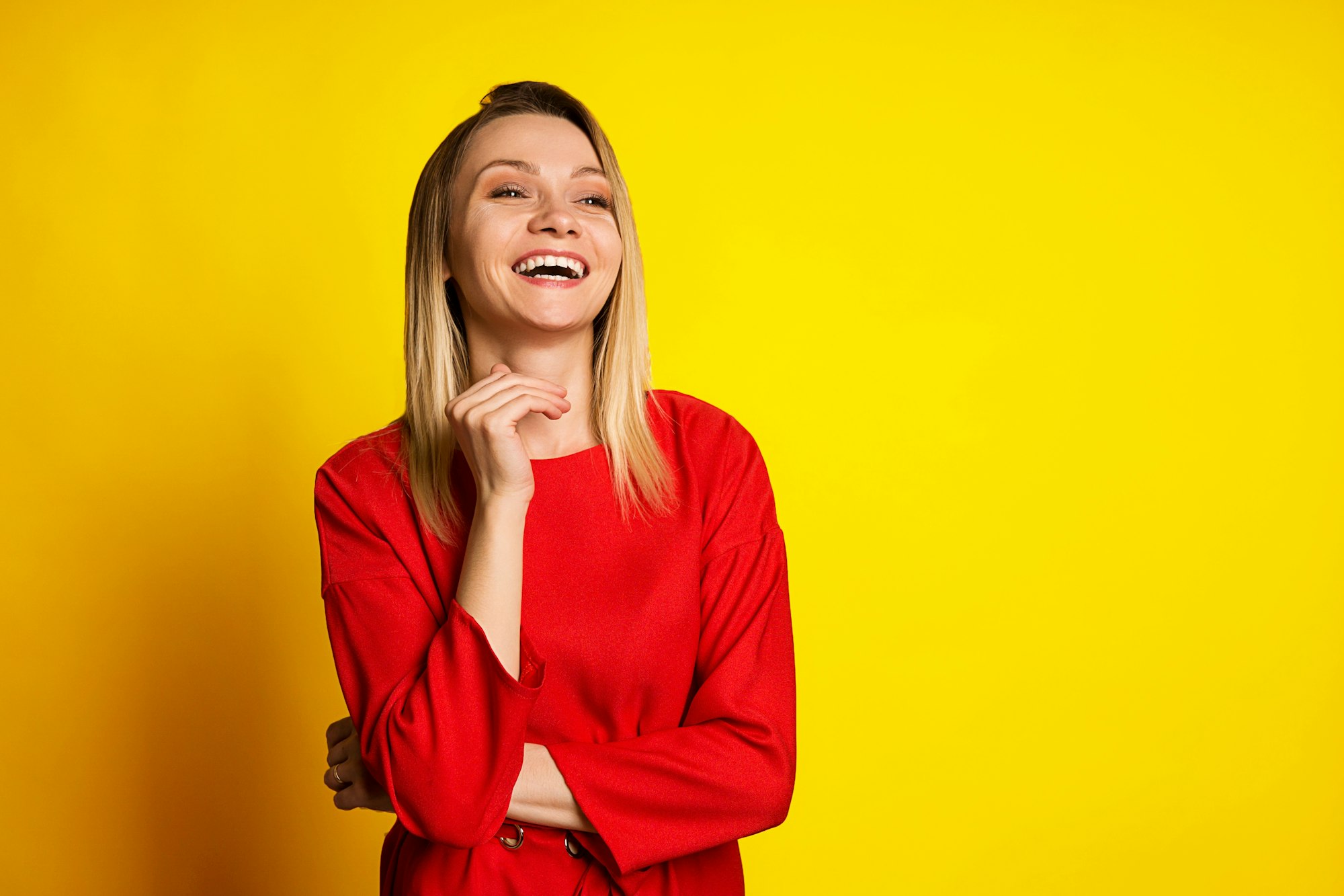 Laughing, happy young girl in a red dress on a yellow background. Space for text, emotional portrait